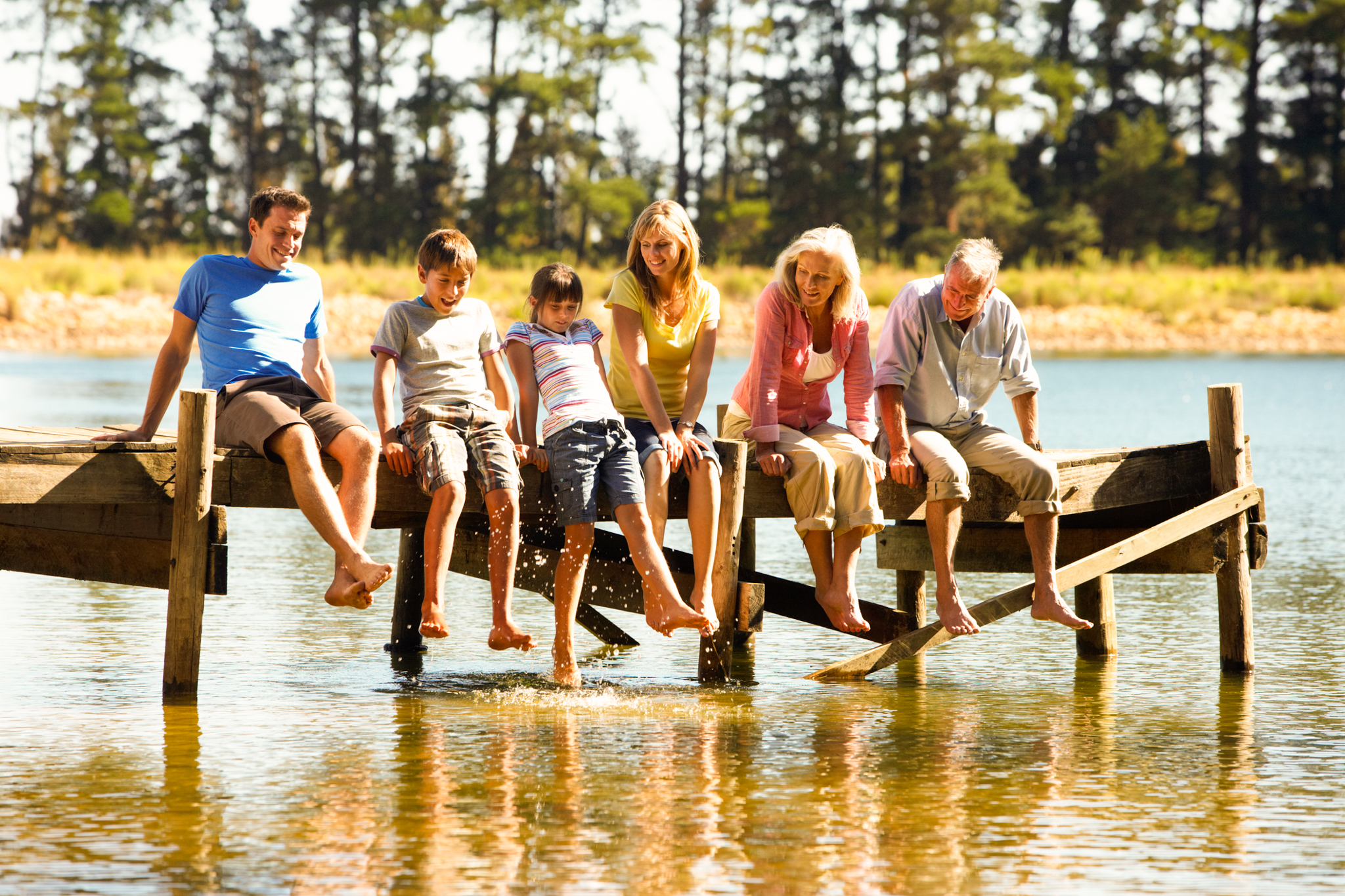 Three Generation Family Sitting On Wooden Jetty